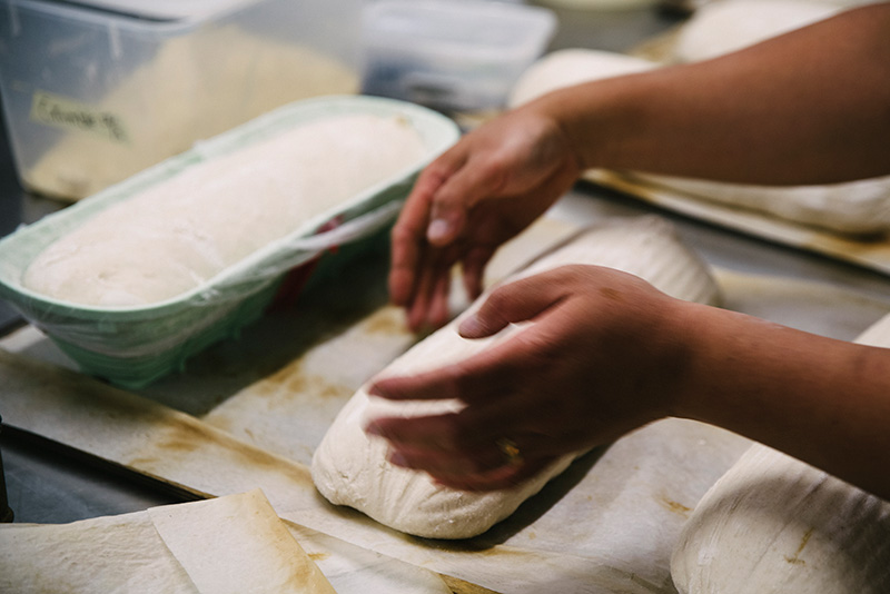 A close up of a baker's hands placing sourdough dough on a tray ready to bake