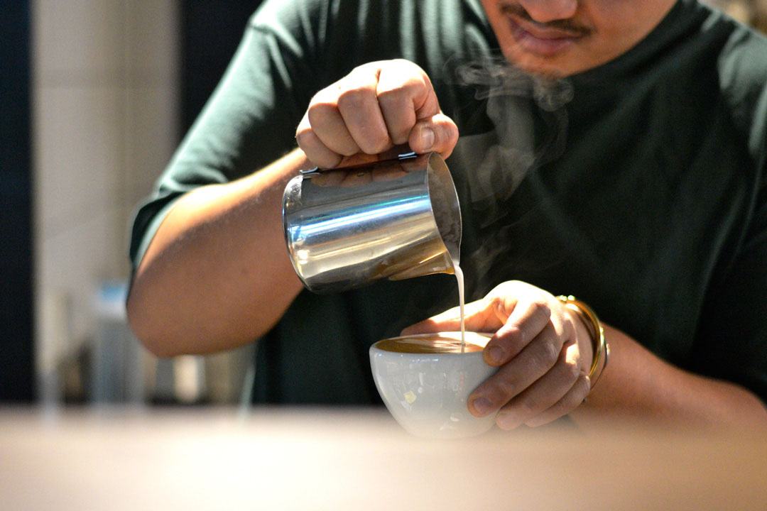 A barista pouring steamed milk into a coffee cup