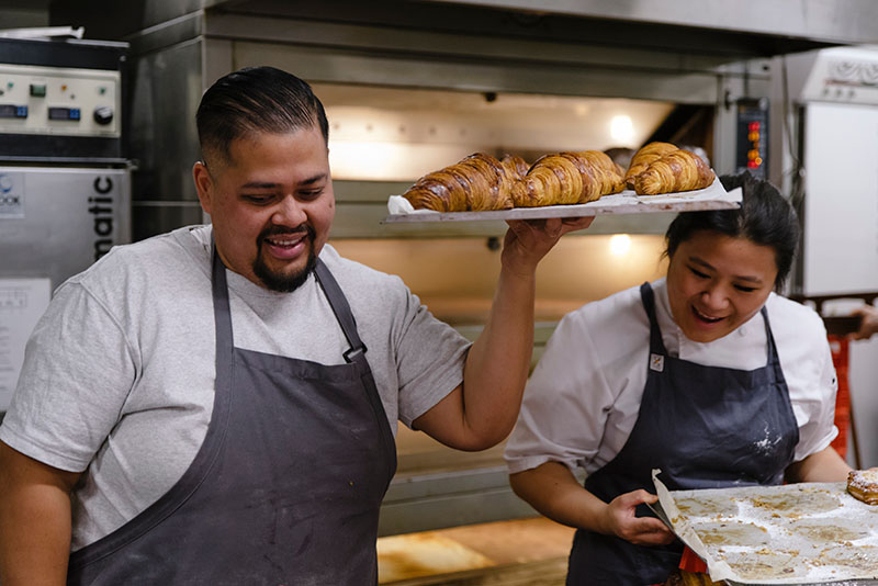 Head baker, Didi, and colleague at STREAT bakery holding a tray of croissants and smiling