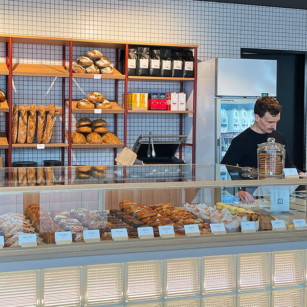 A barista standing next to a bread and pastry display at the STREAT pantry