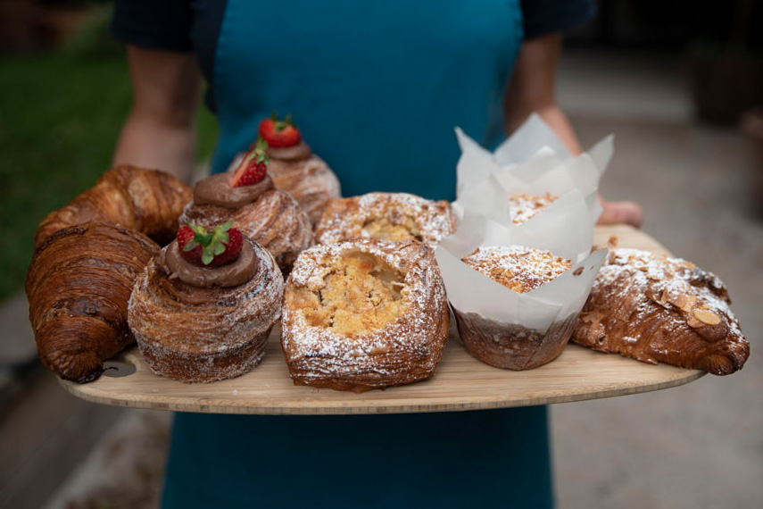 Someone holding a wooden board filled with pastries, muffins and croissants.
